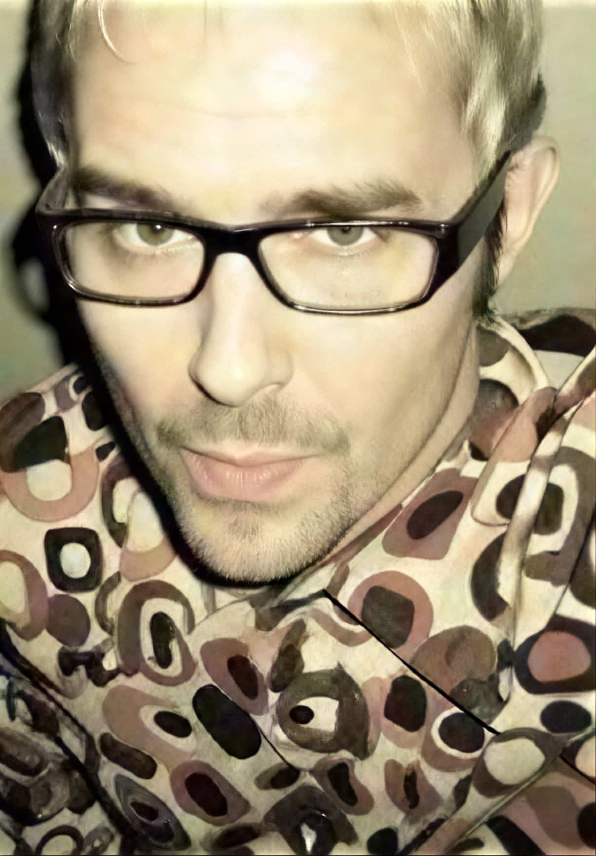 A person with glasses and patterned shirt looking upwards at the camera.