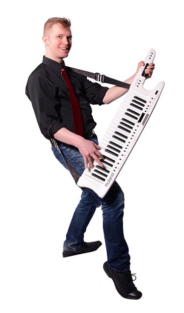 A person playing a white keytar, wearing a black shirt and red tie.