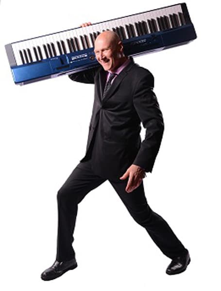 A man in a suit carrying a keyboard on his shoulder against a white background.