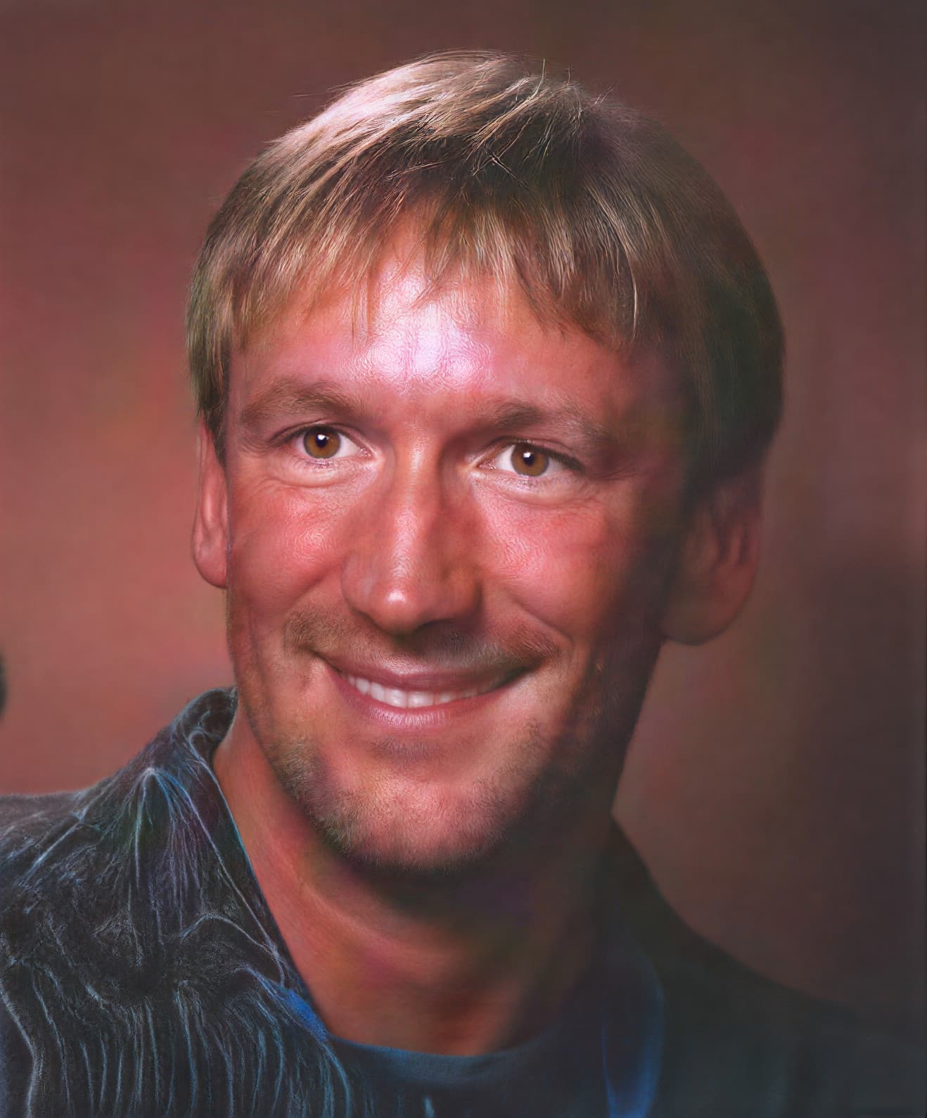 A man with short hair smiling against a brown background.