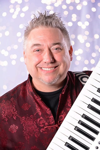 A smiling man with a keyboard against a sparkling background.